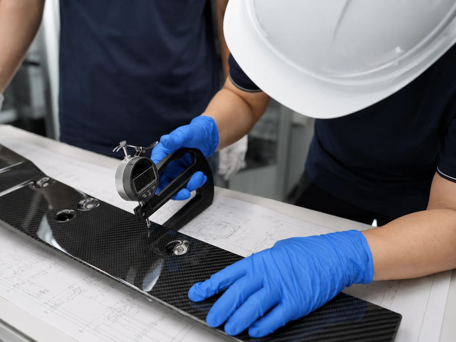 Workers measuring a carbon fiber part against an engineering drawing