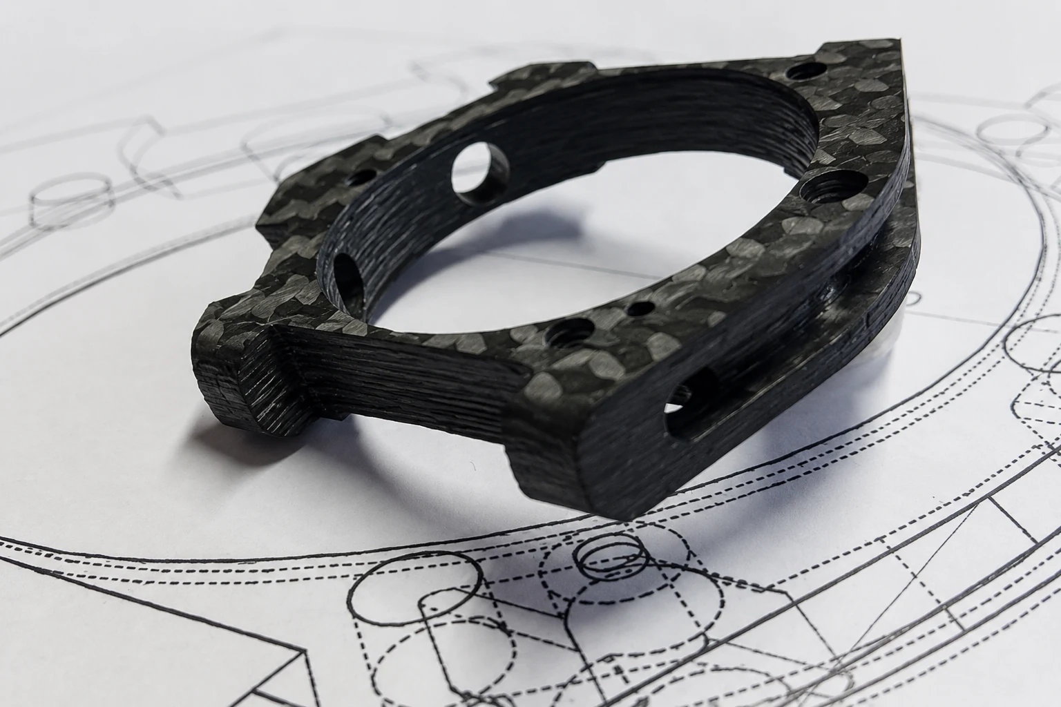 Custom carbon fiber component positioned on an engineering drawing
