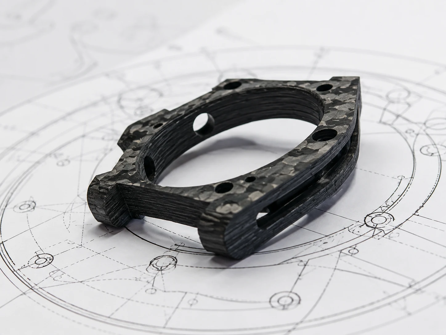 Forged carbon custom component placed over a technical drawing